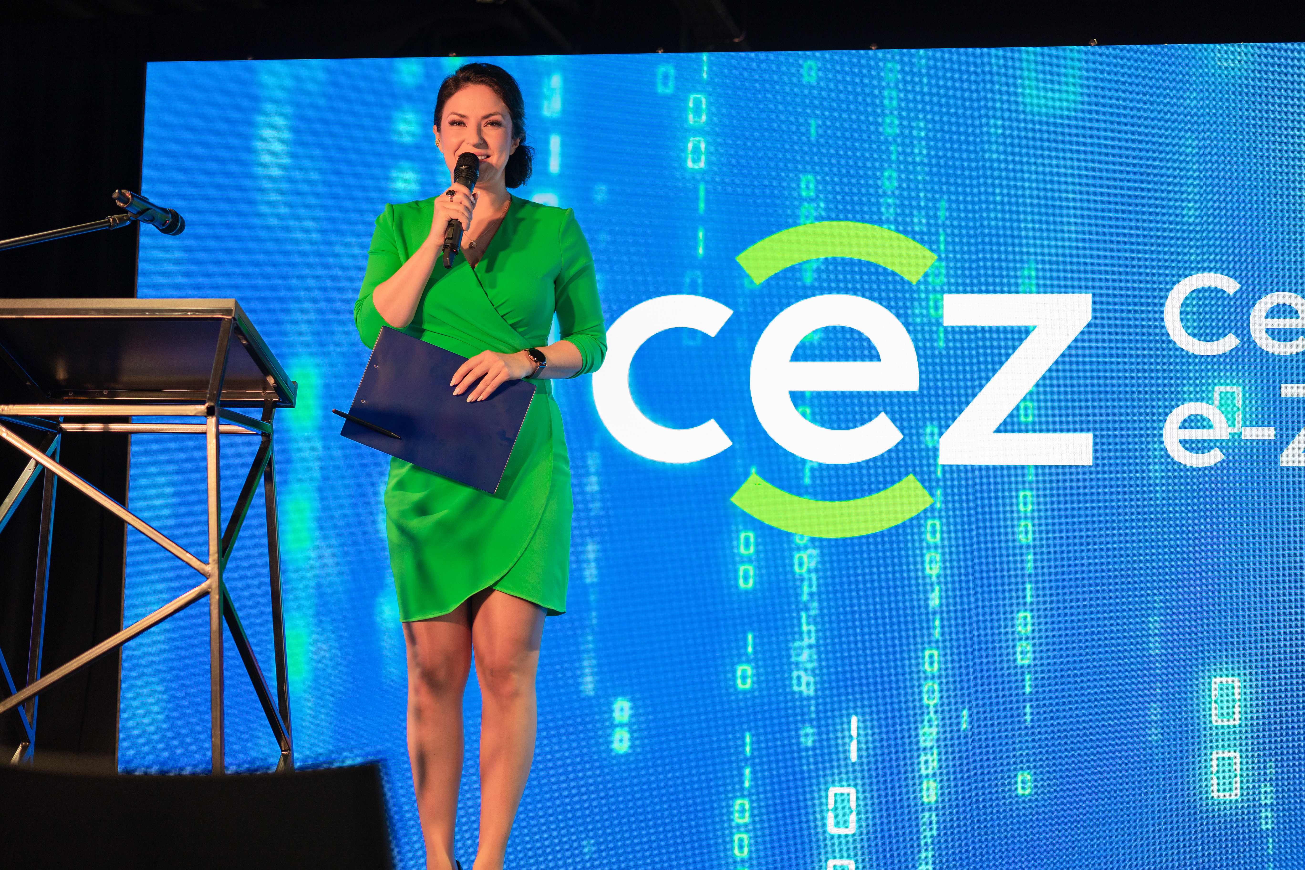 zdjęcie przedstawia stojącą kobietę, trzymającą mikrofon, za nią jest wyświetlane logo CeZ