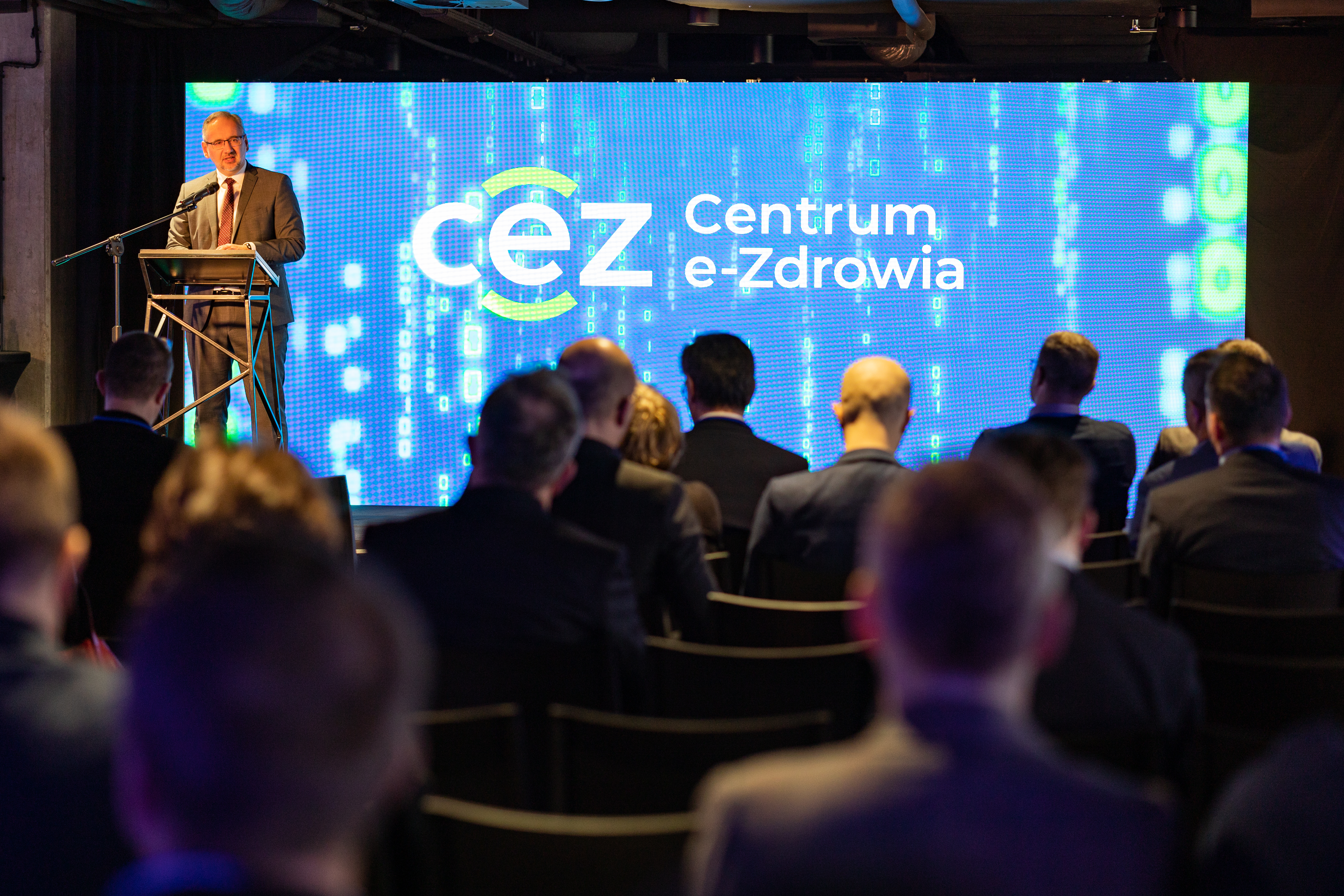 zdjęcie przedstawia mężczyzn siedzących na krzesłach, słuchających wystąpienia osoby stojącej przed nimi