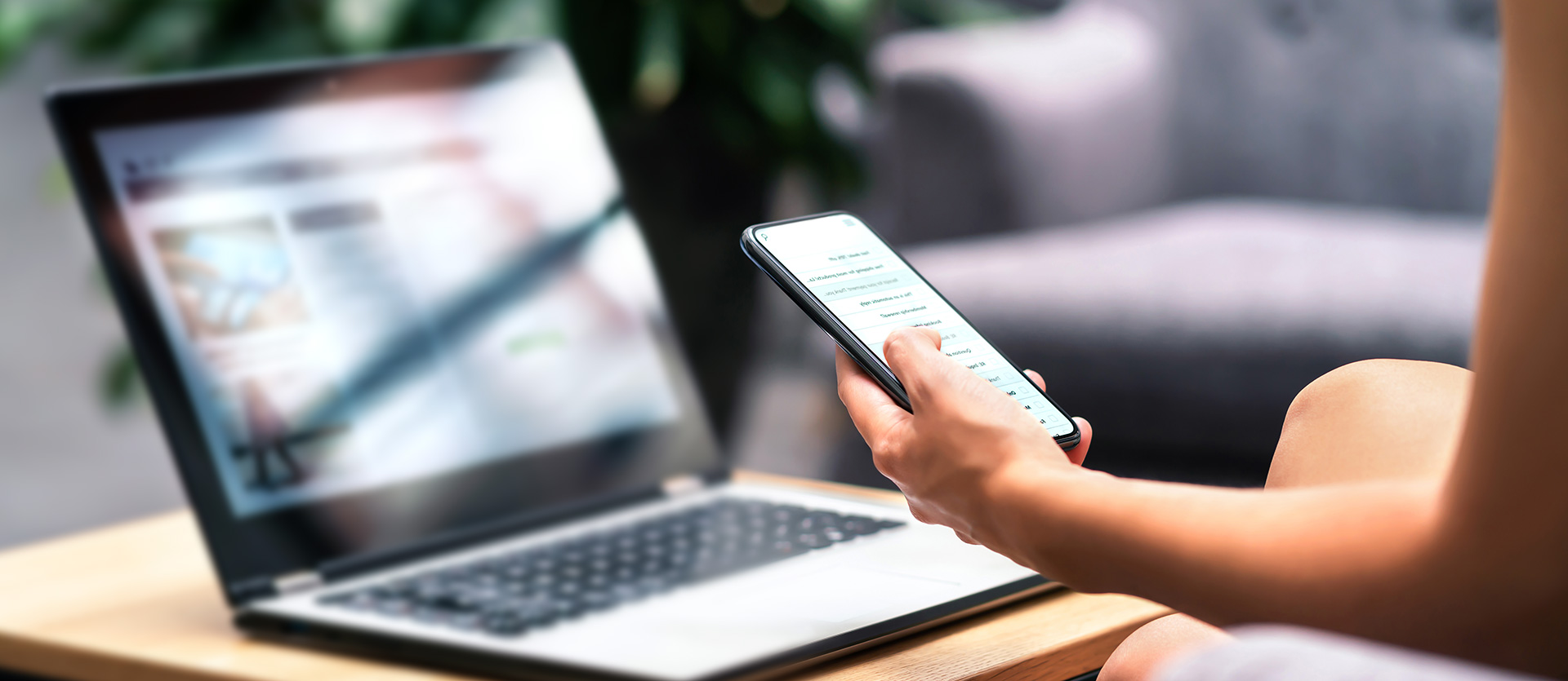 widok dłoni trzymającej smartfona na tle laptopa