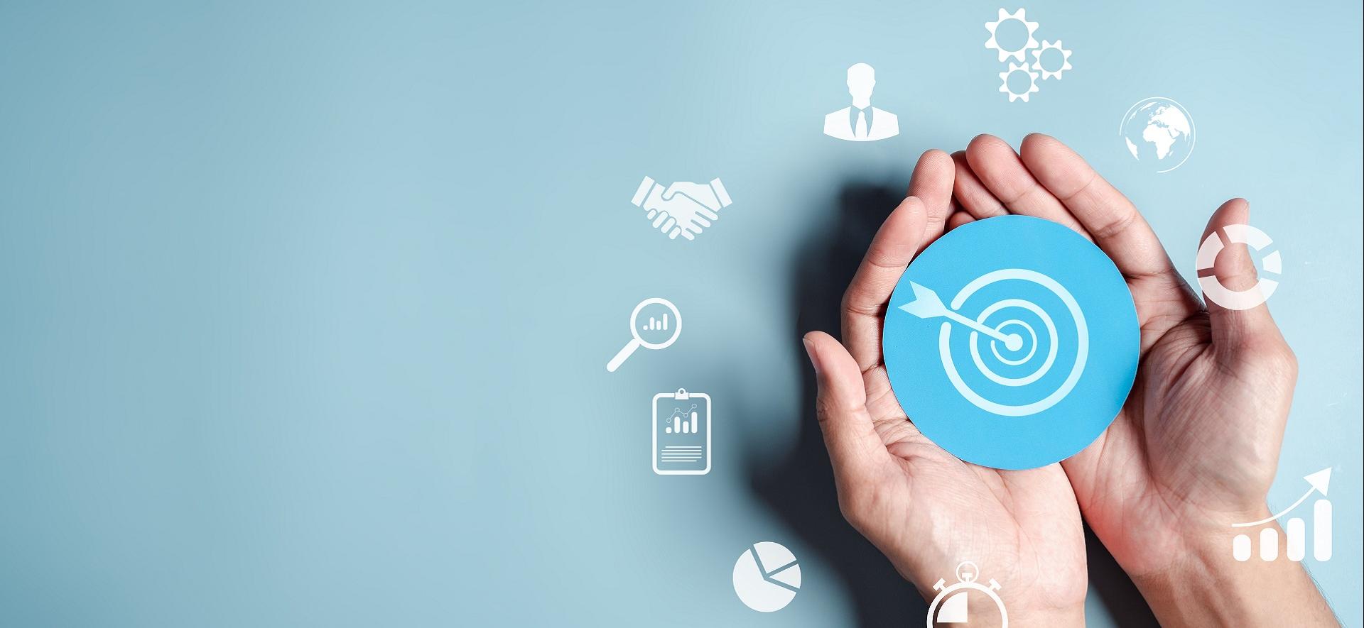 dłonie trzymające grafikę ze znaczkiem strzału w dziesiątkę, wokół infografiki