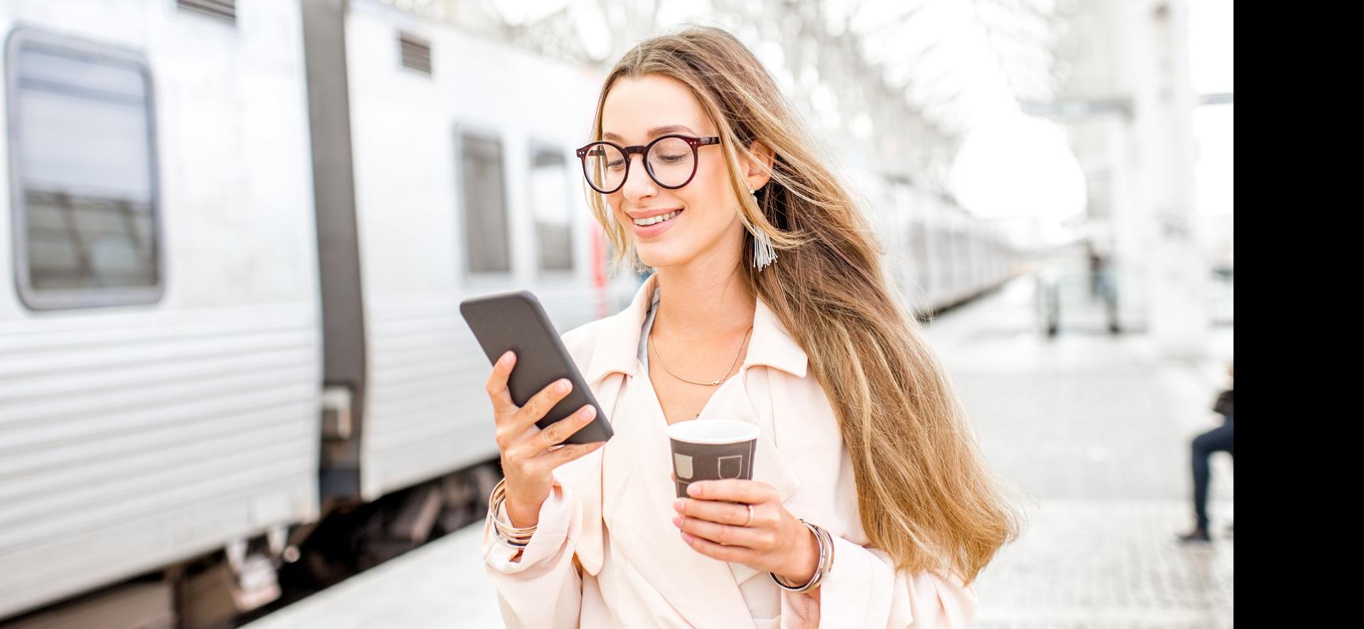 kobieta na dworcu kolejowym trzyma w jednej ręce telefon w drugiej kawę