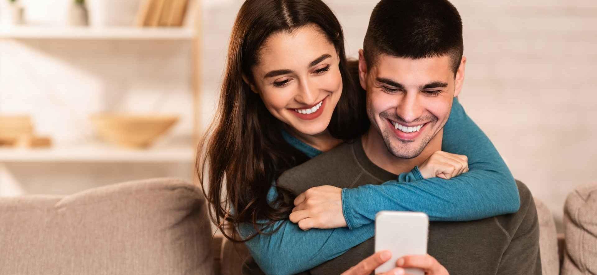 kobieta przytula mężczyznę i wspólnie patrzą się w telefon, który ok trzyma