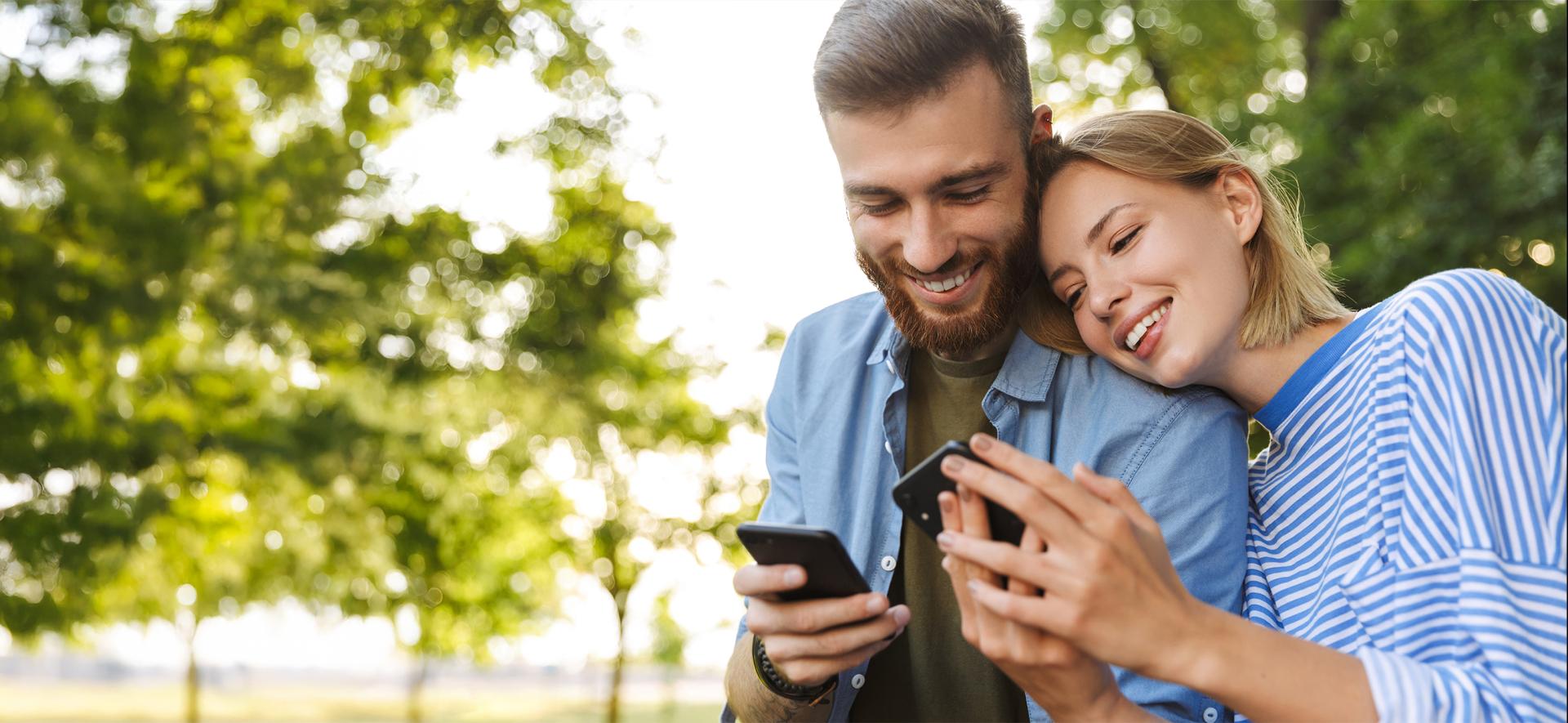 Mężczyzna i kobieta w wieku powyżej 20 lat z uśmiechem patrzą w ekrany telefonów.