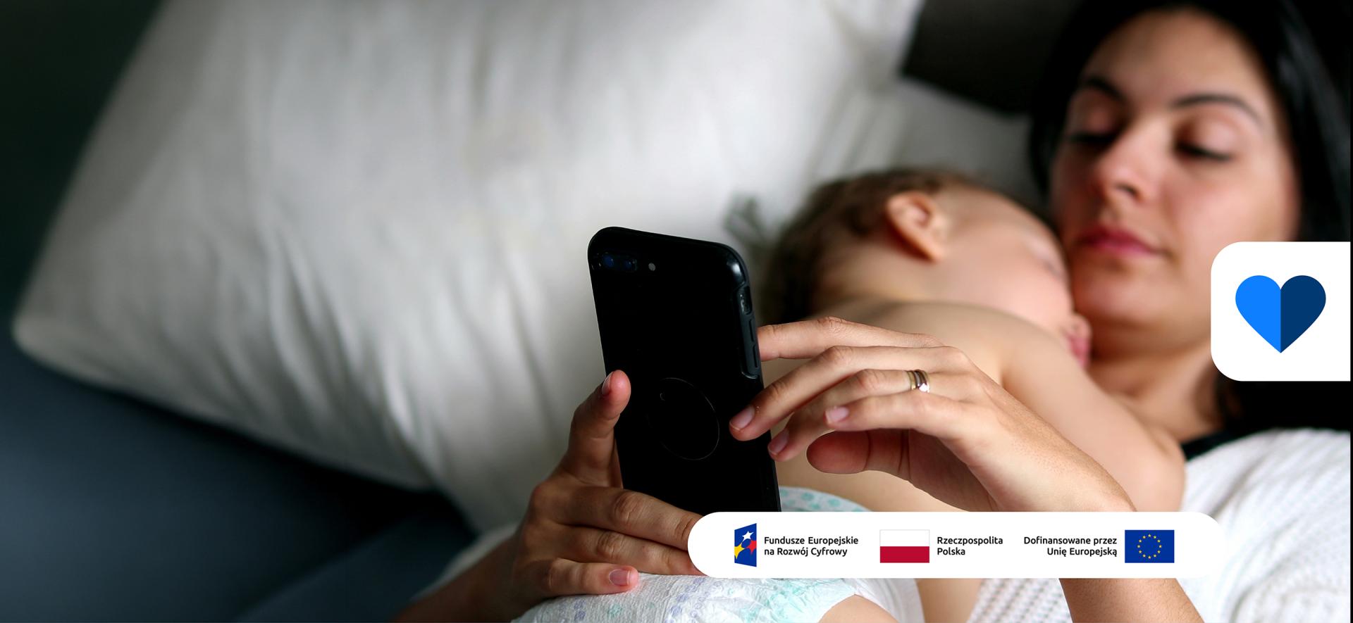 kobieta trzyma smartfona, na niej leży niemowlę