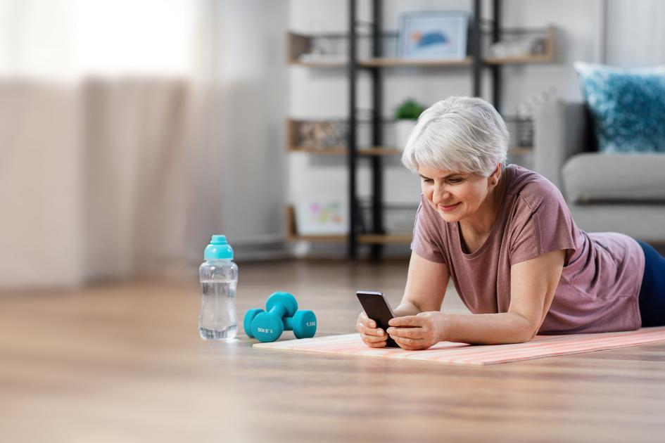 starsza kobieta leżące na macie do ćwiczeń z telefonem w ręku