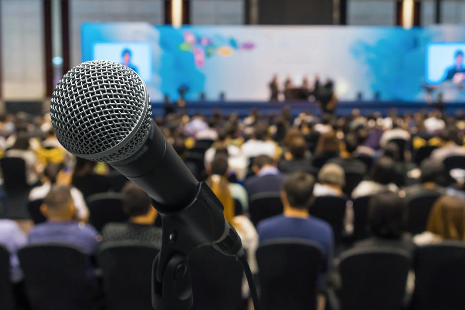 Sala konferencyjna wypełnioną ludźmi, na pierwszym planie jest mikrofon