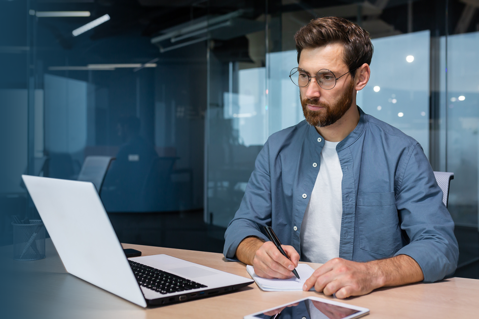 mężczyzna przy komputerze robiący notatki 