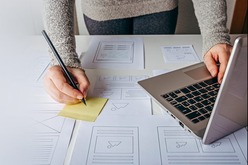 widać ręce osoby, która zapisuje coś na żółtej karteczce, a lewą rękę trzyma na klawiaturze laptopa