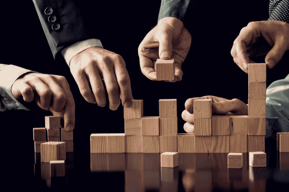 ręce współpracujące nad budową budowli z drewnianych