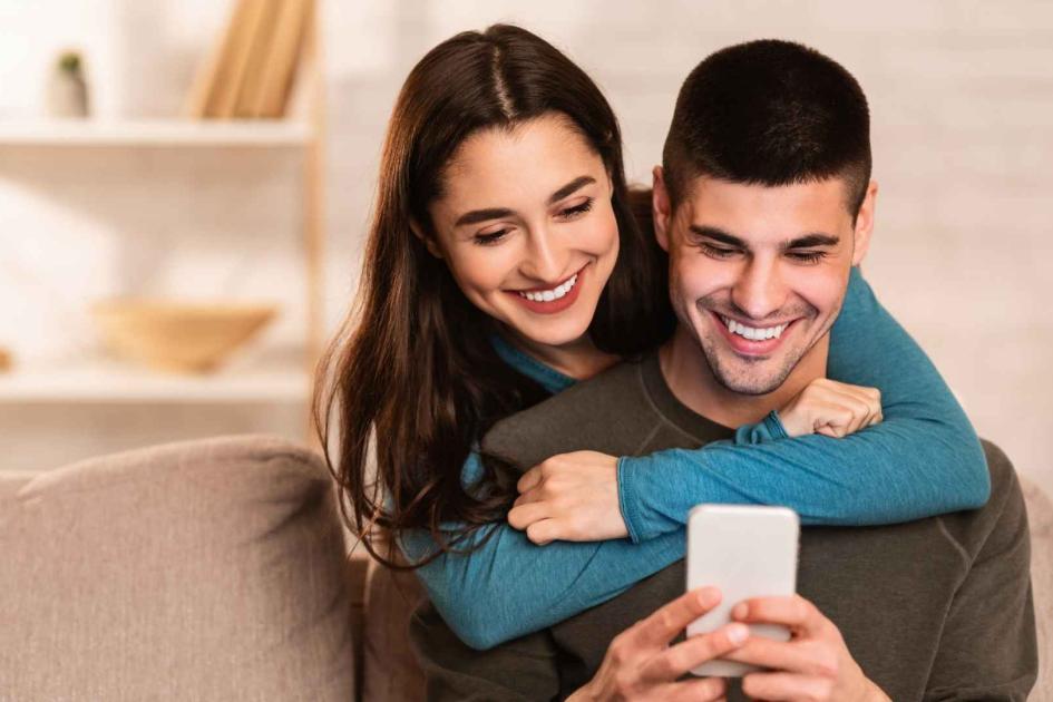 kobieta przytula mężczyznę i wspólnie patrzą się w telefon, który ok trzyma