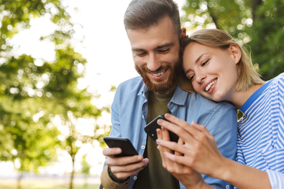 Mężczyzna i kobieta w wieku powyżej 20 lat z uśmiechem patrzą w ekrany telefonów.