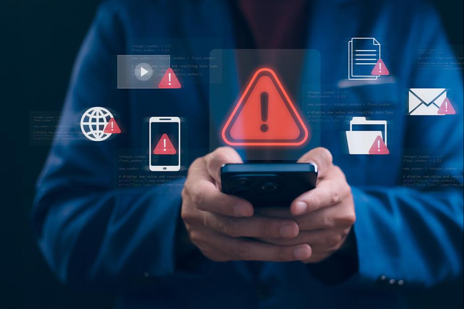 człowiek trzyma telefon, a nad nim unosi się ikona czerwonego trójkąta z wykrzyknikiem