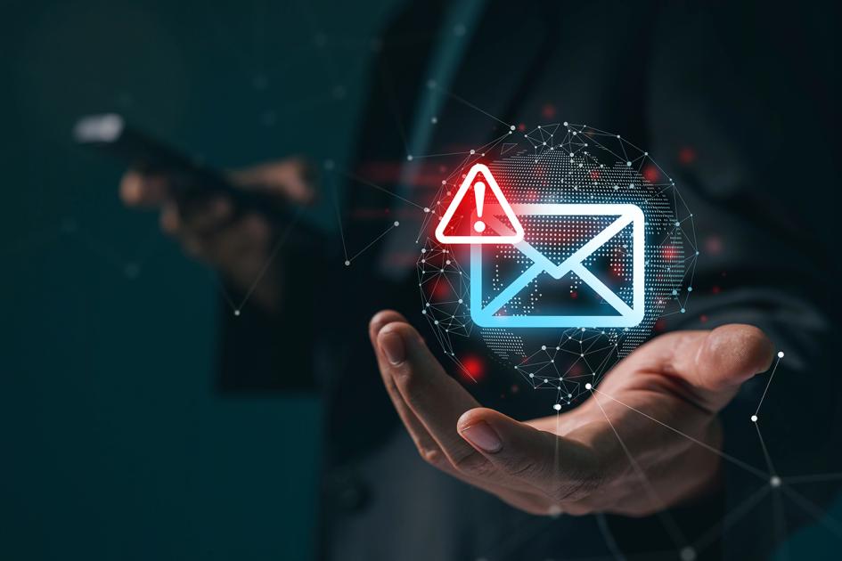 nad ręką unosi się niebieski neon w kształcie koperty z czerwonym trójkątem z wykrzyknikiem w rogu