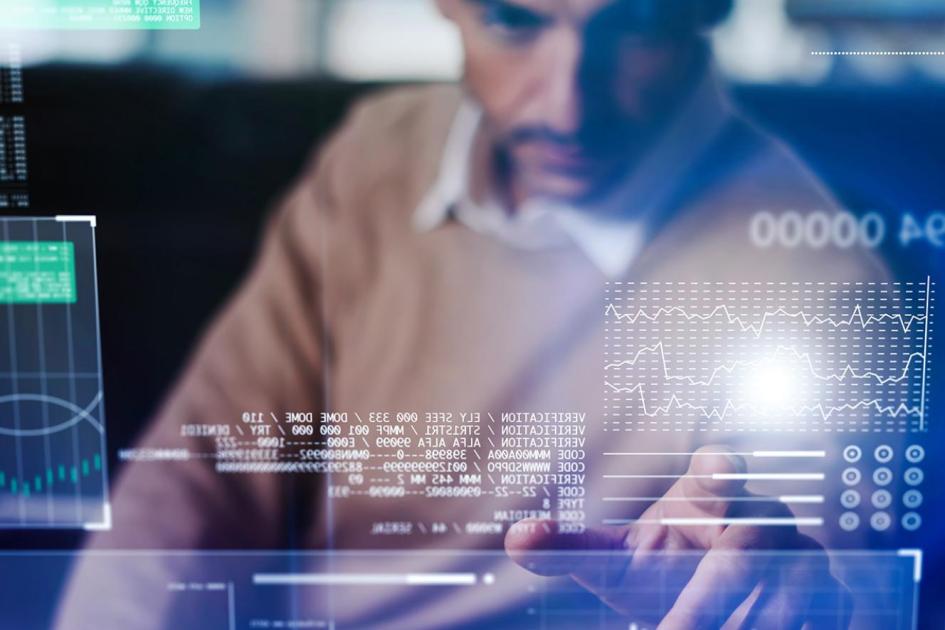 na pierwszym planie napisy i ikony informatyczne a na drugim planie mężczyzna korzystający z komputera